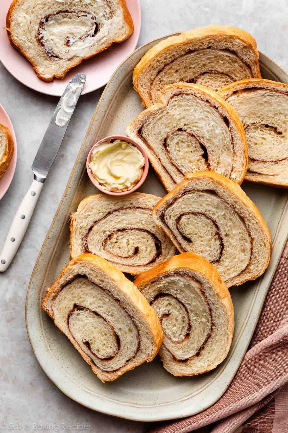 slices of homemade cinnamon swirl yeasted bread slices on gray platter with pink dish of butter.