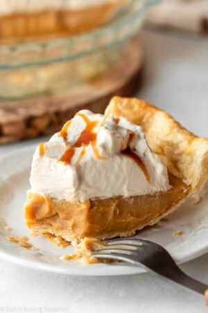 slice of butterscotch pie with whipped cream on top with fork bite taken out of the end.