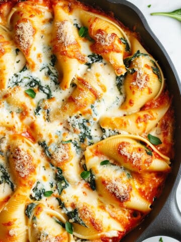 Spinach and ricotta stuffed shells in a skillet baked with cheese.