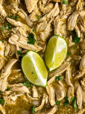 Close up of salsa verde chicken in a Crock Pot with garnished with cilantro and limes.