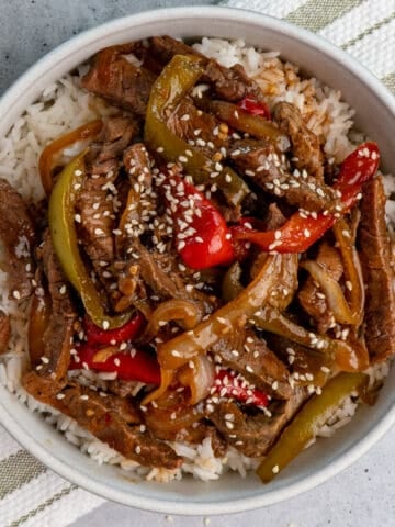 Crock pot pepper steak over white rice in a bowl.