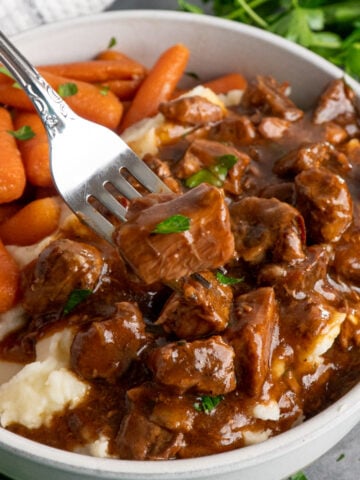 A fork holding holding a piece of crock pot beef tips and gravy over a bowl.