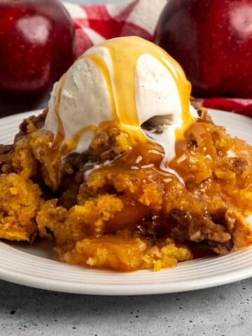 Plate of crock pot apple cobbler with ice cream and caramel on top.