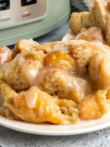 Crock pot bread pudding on a white plate in front of a green slow cooker.