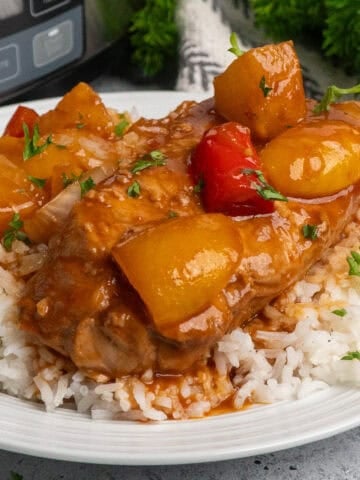 Hawaiian pork chops on a plate of rice with a slow cooker in the background.