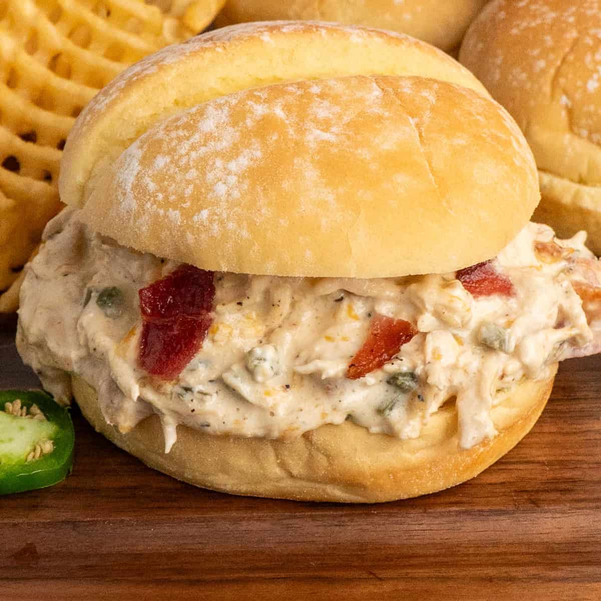 A crock pot jalapeno popper chicken sandwich on a wood cutting board.