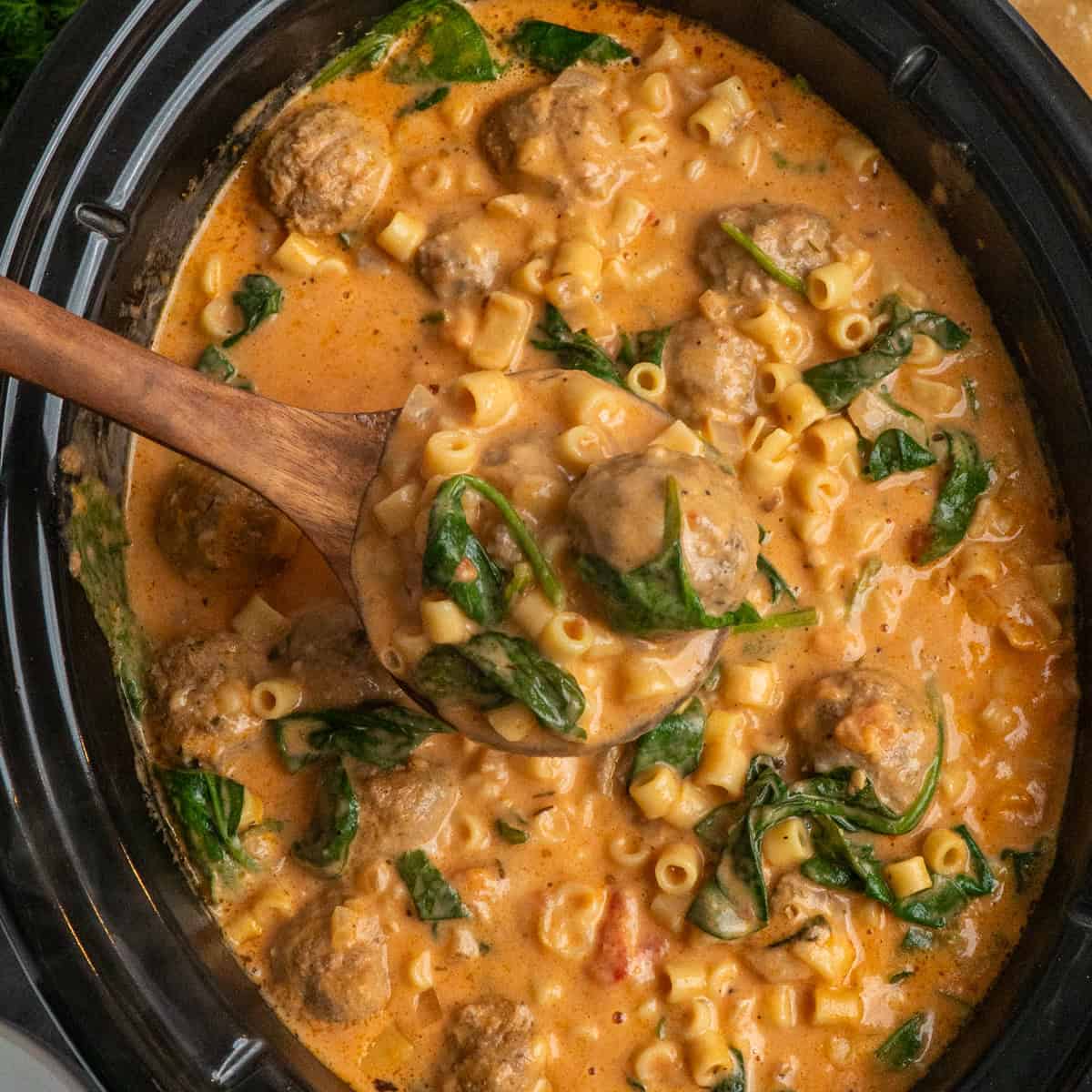 A wooden ladle holding a serving of slow cooker meatball soup.