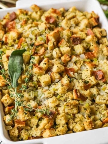 Overhead view of a casserole dish of stuffing topped with a bundle of fresh herbs.