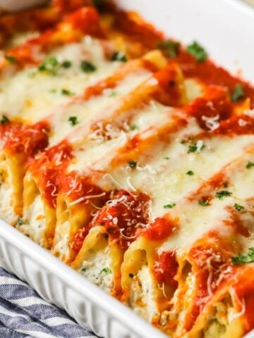 Manicotti in a casserole dish topped with sauce and cheese.