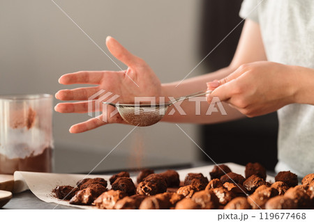 young woman sprinke truffles candy with cocoa powder on kitchen 119677468