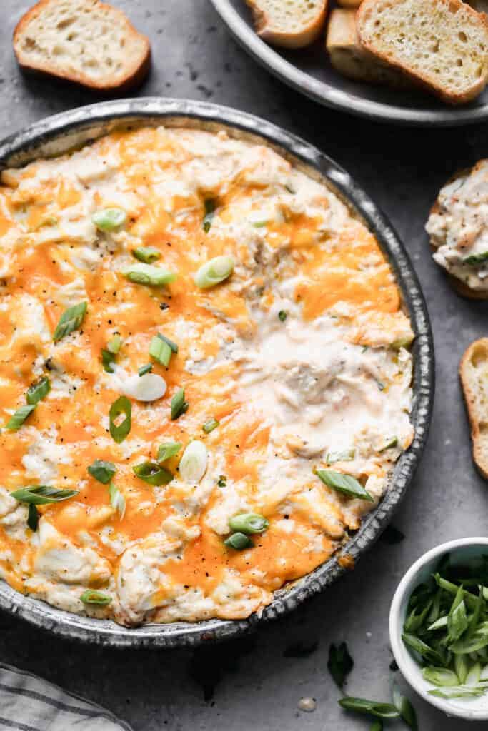 Hot crab dip baked in a round baking dish with cheese on top, and bread slices on the side for dipping.