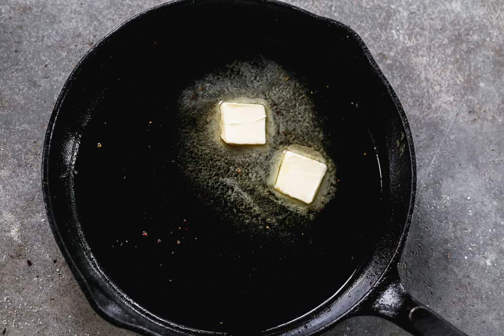 A cast iron skillet with oil and butter heating in it.