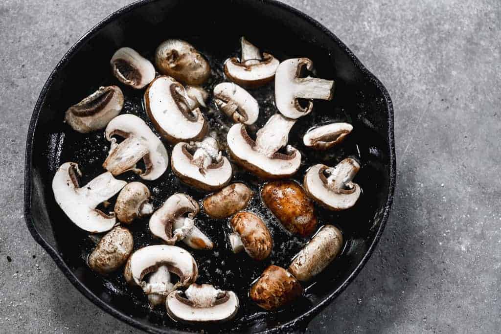 Mushroom slices in a hot pan, in a single layer, spaced apart.