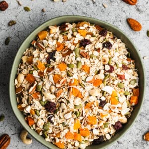 A homemade Muesli recipe in a big green bowl with oats, dried fruit, nuts, and pumpkin seeds.