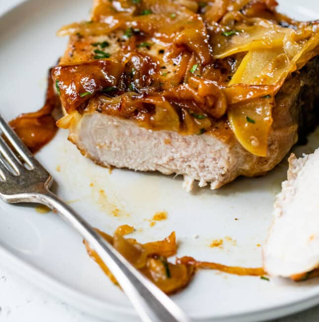 apple pork chops on a plate with a fork and with a portion of the pork chop cut off