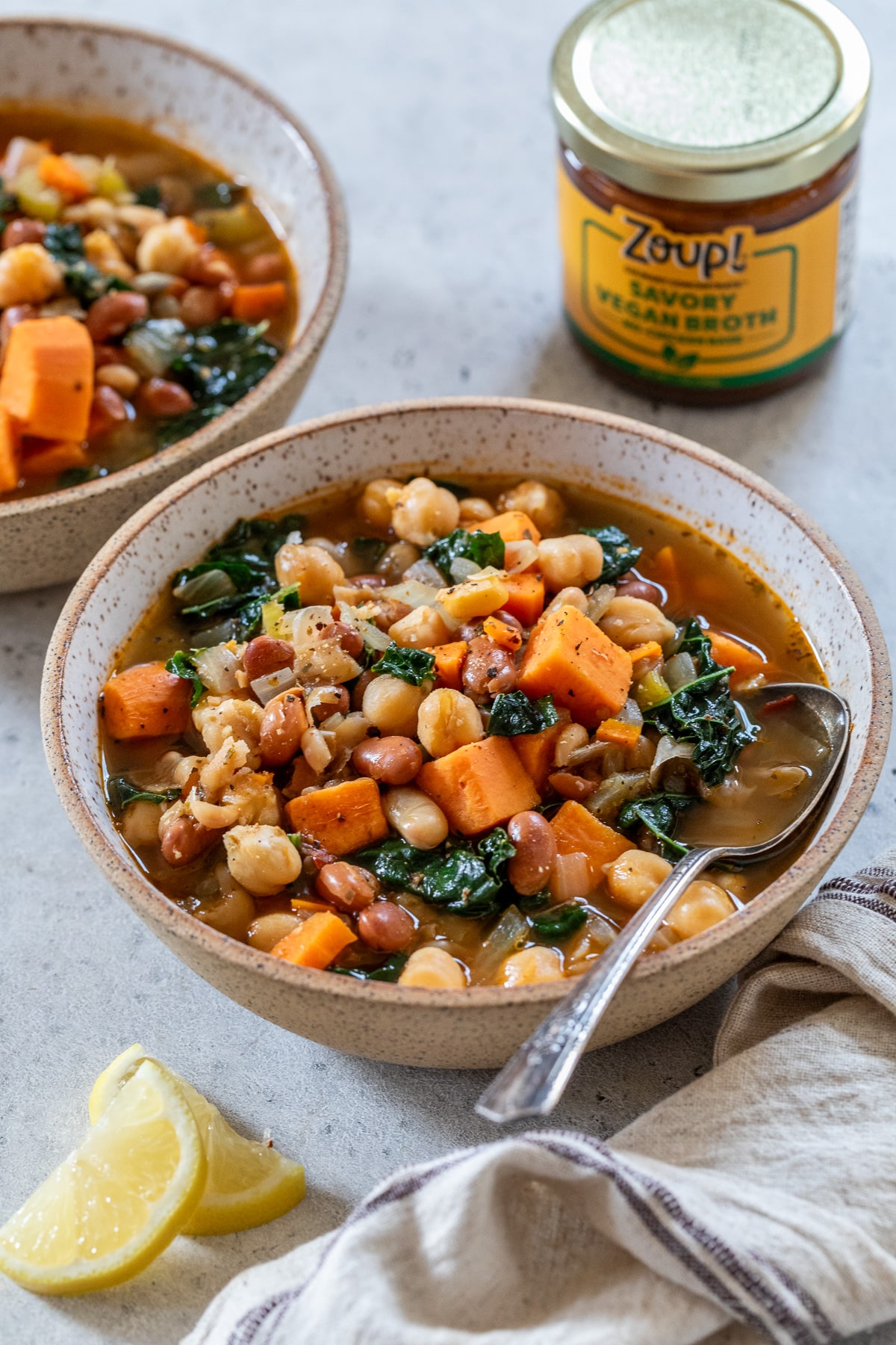 two bowls of soup with vegetables and beans beside some cut lemon slices