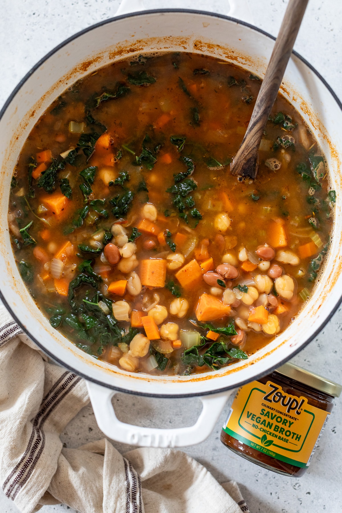 soup in a dutch oven with a wooden spoon beside a jar of vegan broth