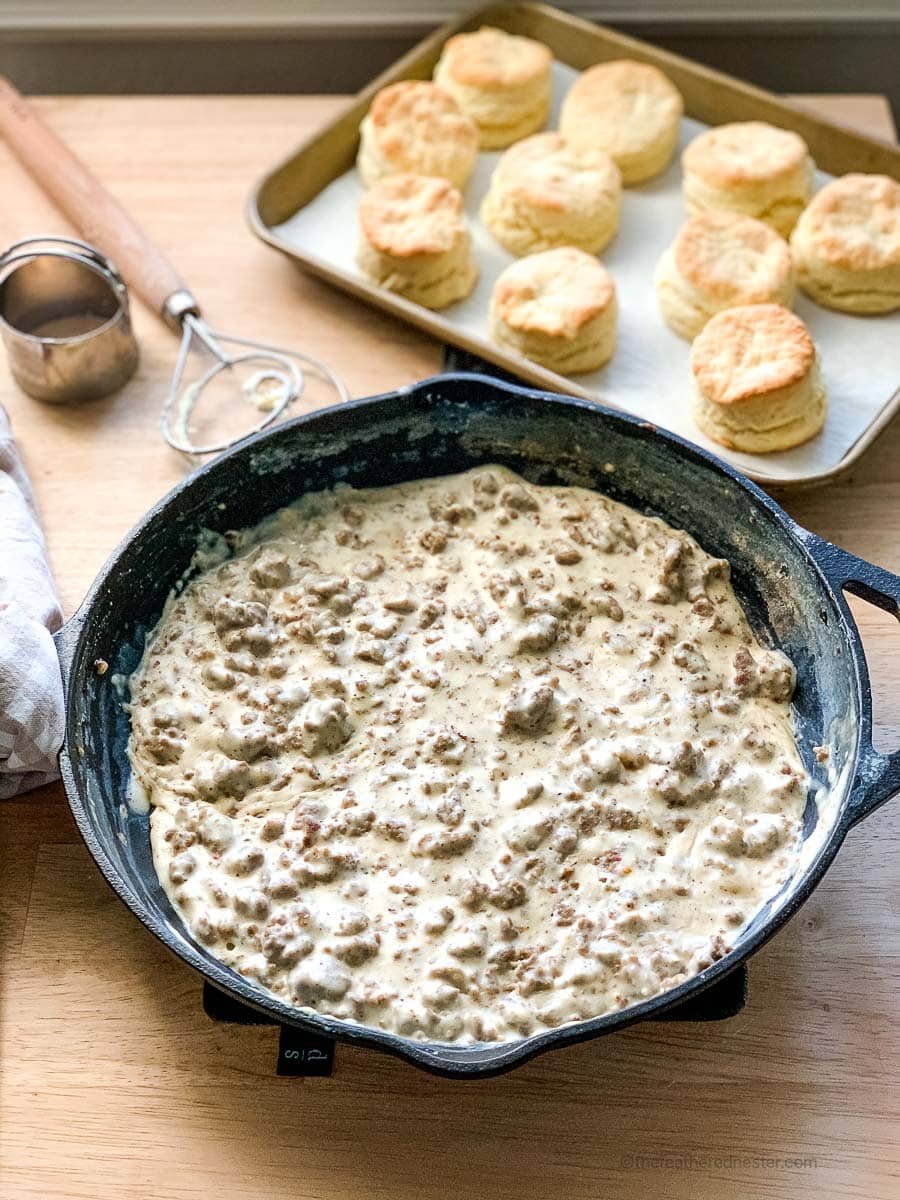 a cast iron skillet of gravy sausage with a pan of biscuits in the background.