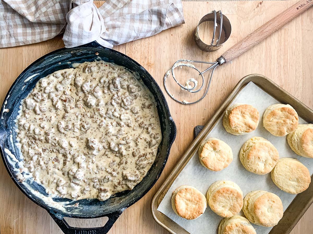 a cast iron skillet of gravy sausage with a pan of freshly baked biscuits.