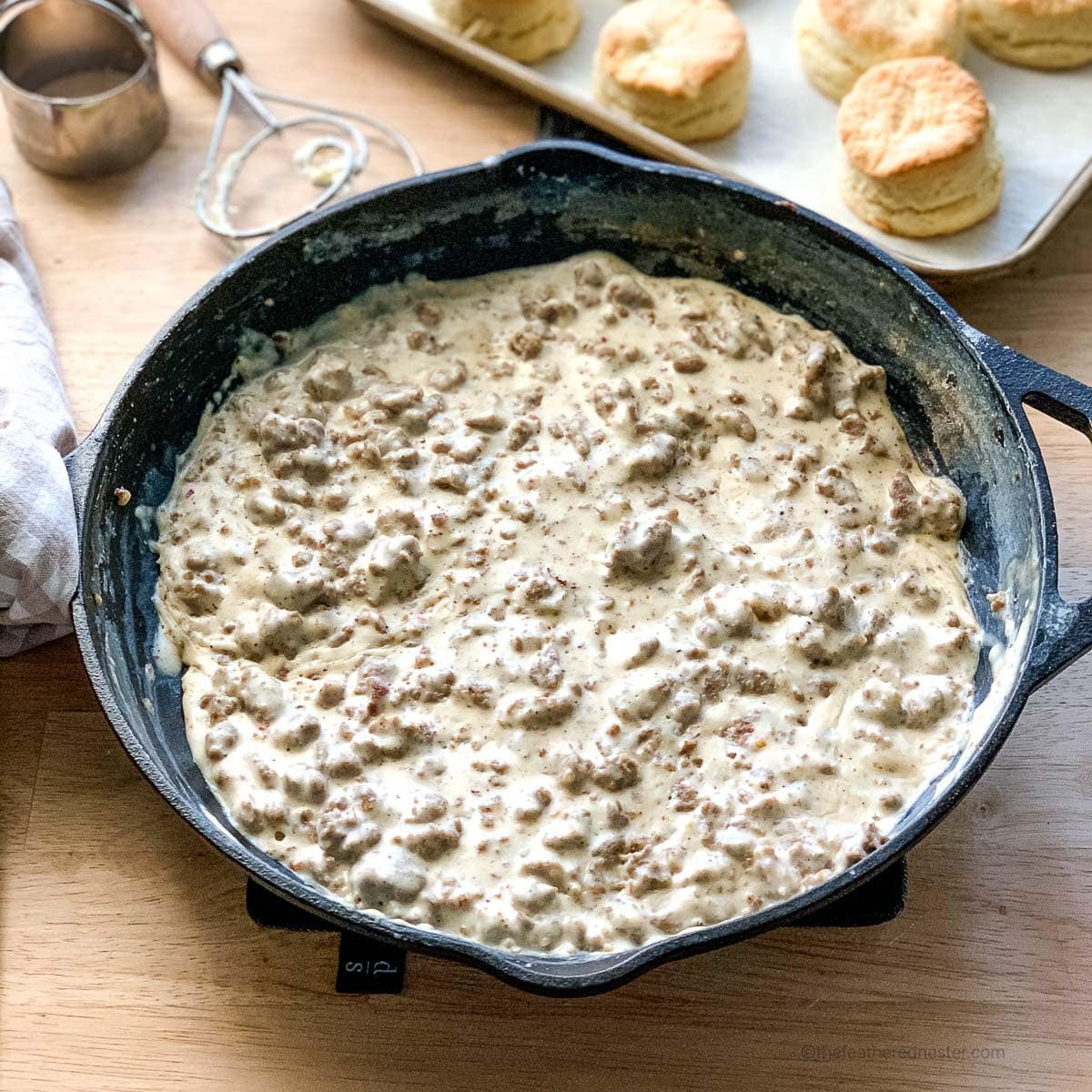 a cast iron skillet of gravy sausage with a pan of biscuits in the background.