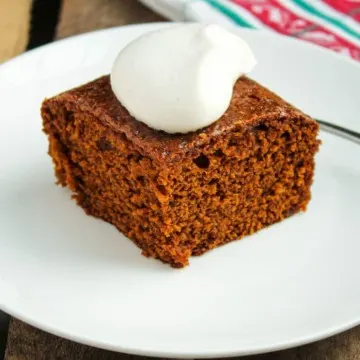 Piece of gingerbread with whipped cream on white plate.