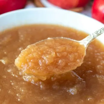 Spoonful of applesauce over white serving bowl.