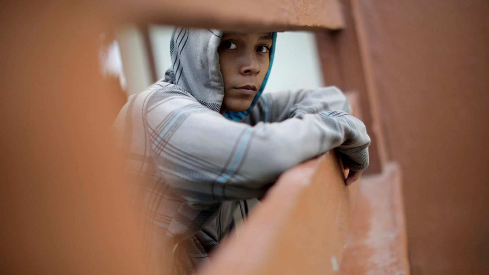 A young man waits for a ride, looks at the camera.