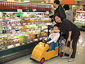 Child in a toy vehicular attachment to a shopping cart