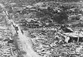 A column of Marine infantry and vehicles push through the street of a Tinian town, reduced to rubble by the fighting. July-August 1944.