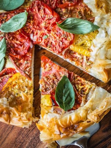 Cheese and tomato pie on a wooden board garnished with basil.