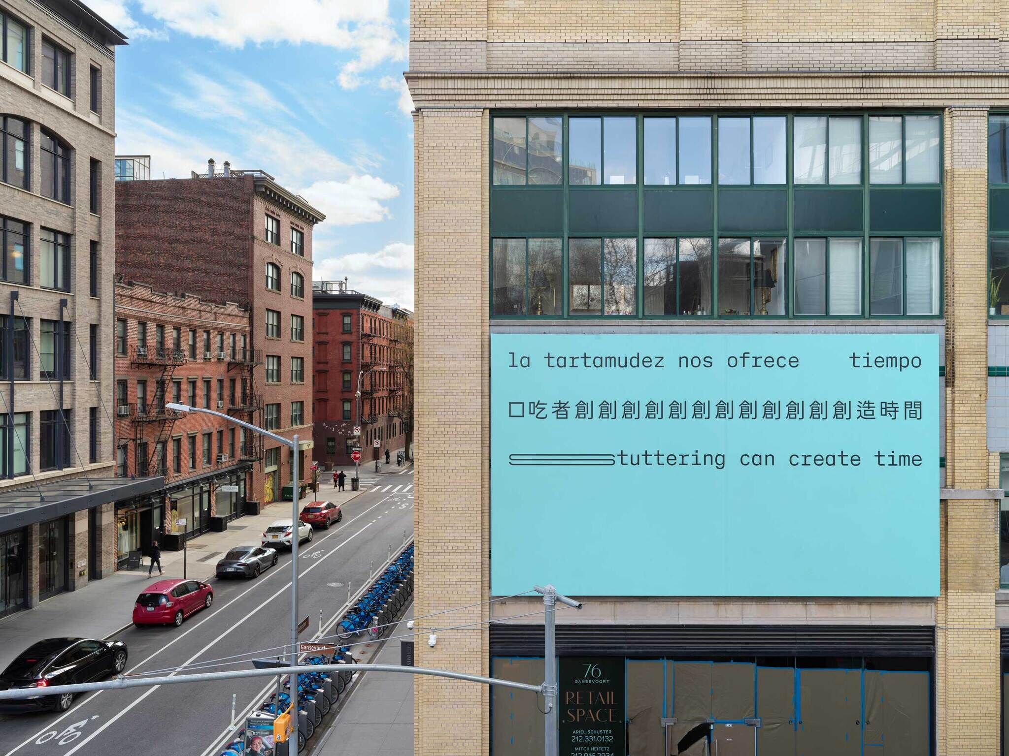 A large billboard is displayed on the facade of a beige brick building at 95 Horatio Street, across from the Whitney Museum and the south end of the High Line. The billboard is part of the Whitney Biennial 2024: Even Better Than the Real Thing and is presented by the collective People Who Stutter Create (PWSC). The billboard has a light blue background and features the phrase "stuttering can create time" in three languages: Spanish, Chinese, and English.

The text is black and positioned in three distinct lines. The first line reads "la tartamudez nos ofrece tiempo" in Spanish, the second line is in Chinese characters, and the third line reads "stuttering can create time" in English. Each line is evenly spaced, with the Chinese text having a repeated character sequence that creates a rhythmic visual pattern.

The surrounding area includes a row of brick buildings in various shades of brown and red, with black fire escapes visible on the sides. There is a street below with parked cars, including a white truck and several other vehicles, and a blue bike-sharing station. The street is wet, indicating recent rain, and the sky is overcast with gray clouds. 