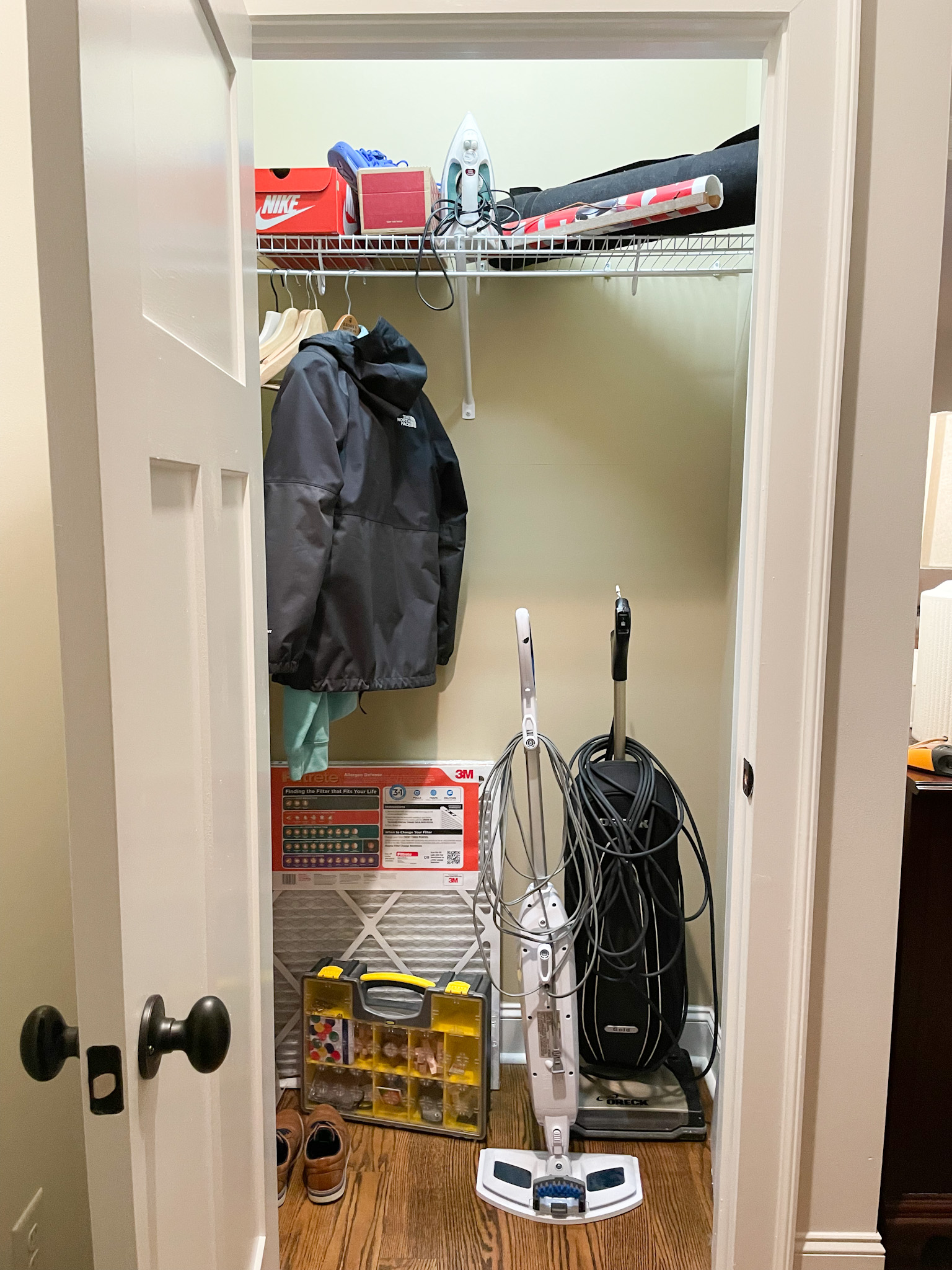 open messy closet with vacuum, mop and hanging coat