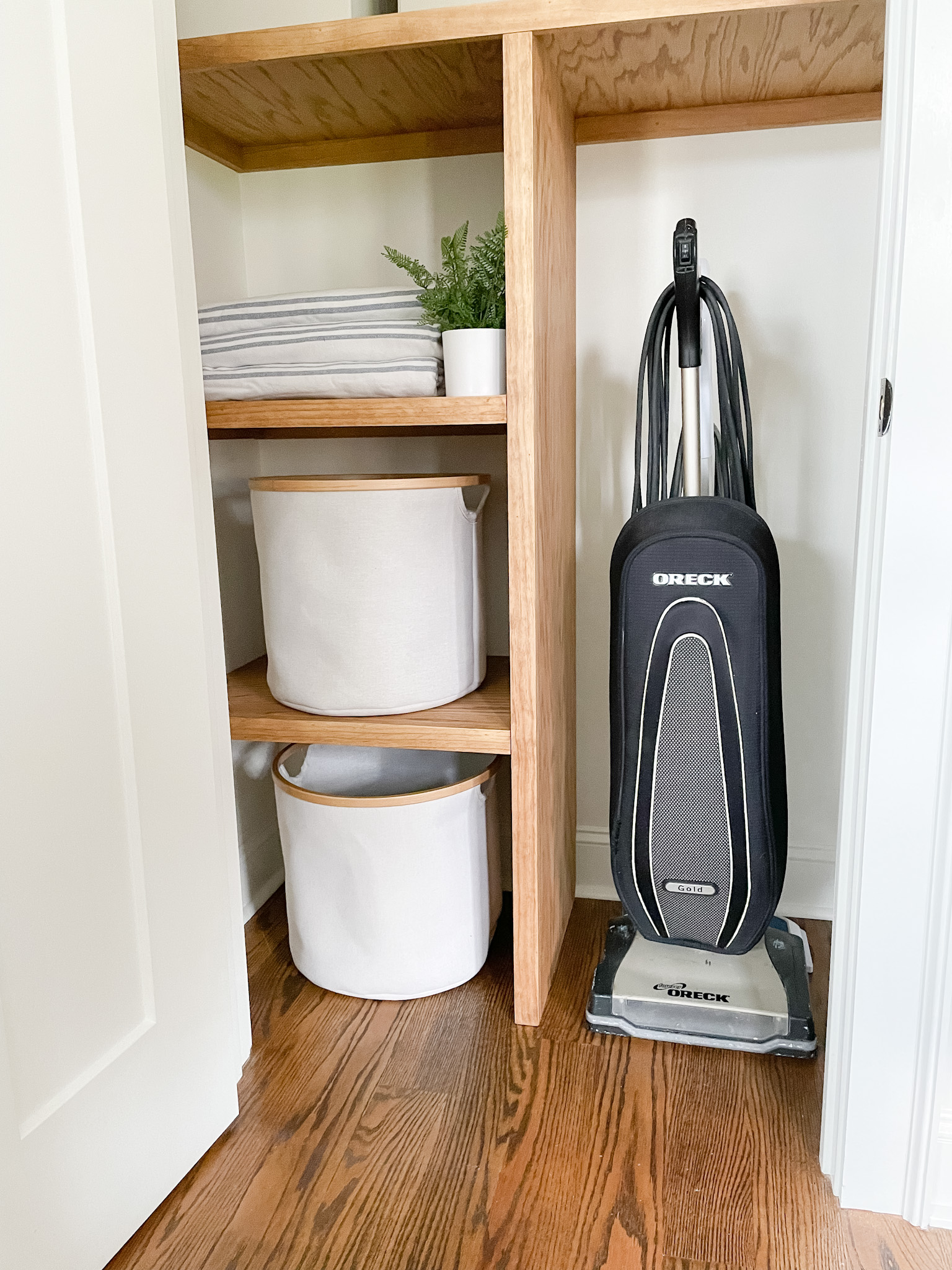 wood shelves in closet with storage bins, towels and vacuum. 