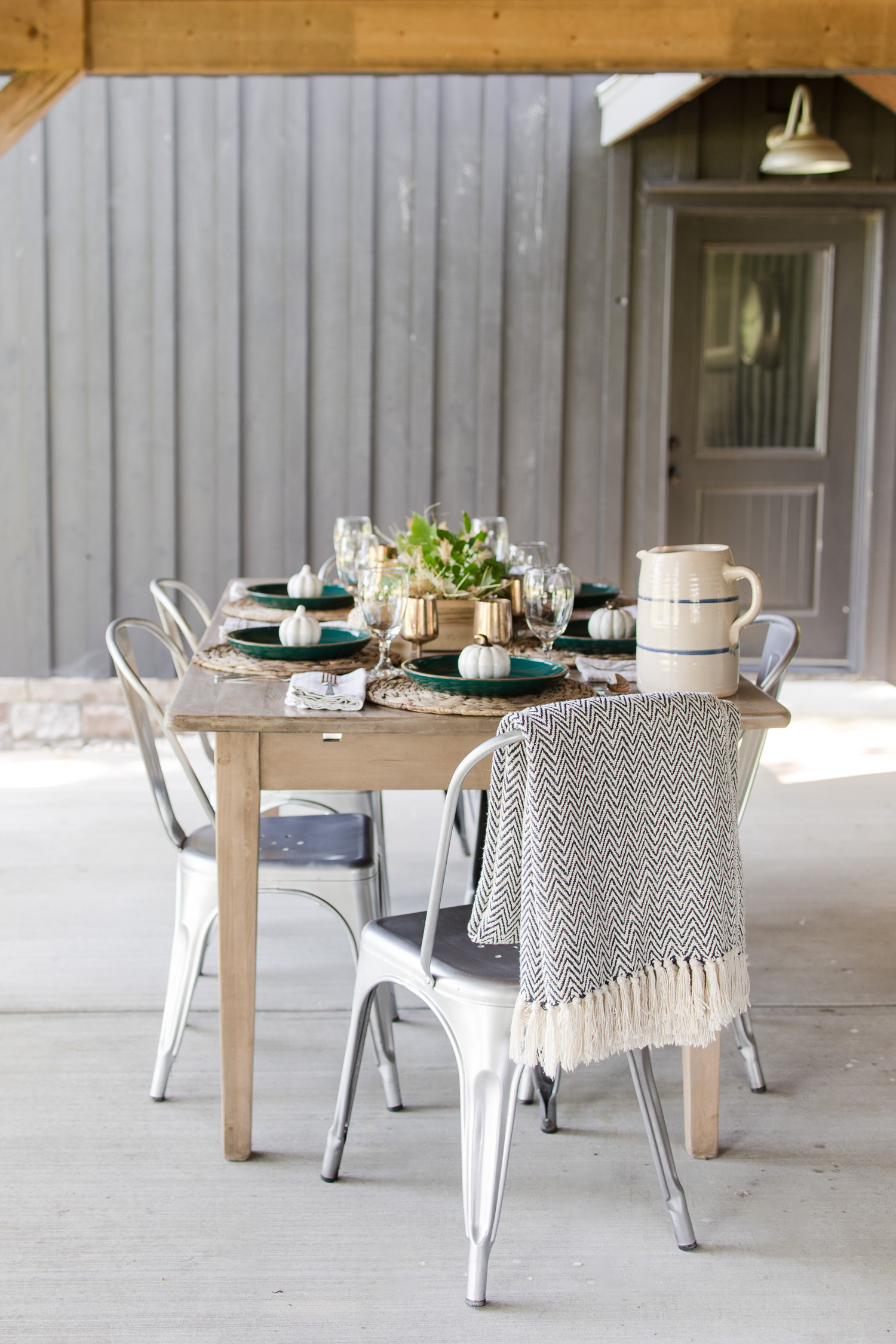 fall tablescape on the outdoor back patio with green plates, wooden table, silver metal chairs, pumpkins and brass goblets