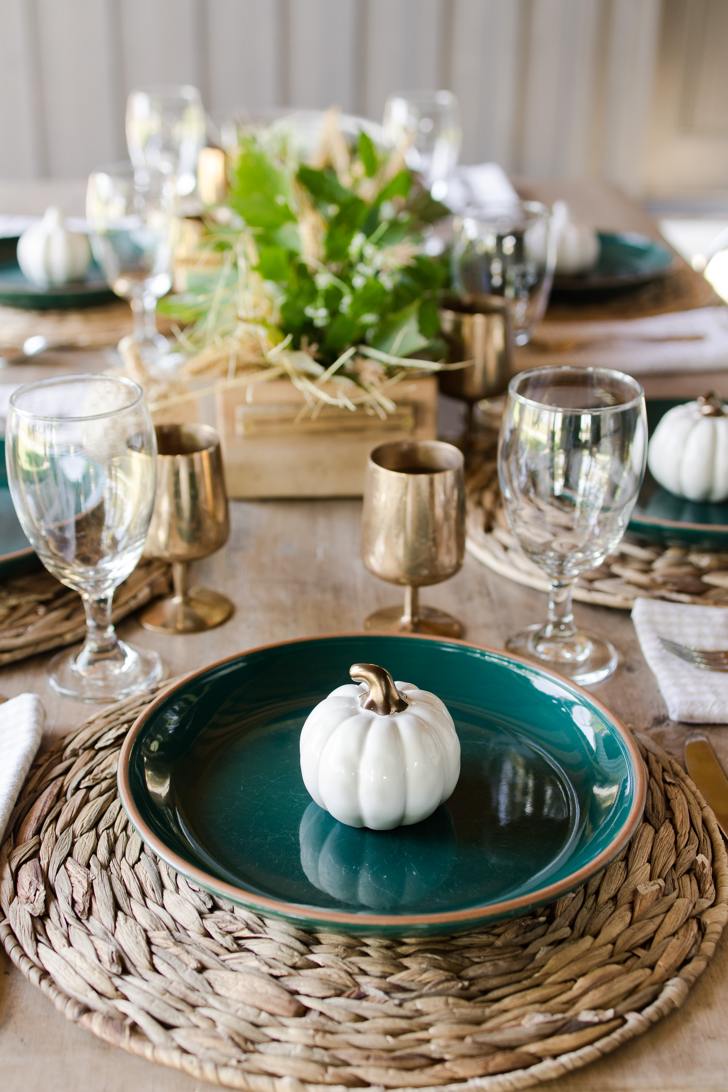 fall tablescape on the outdoor back patio with green plates, wooden table, silver metal chairs, pumpkins and brass goblets