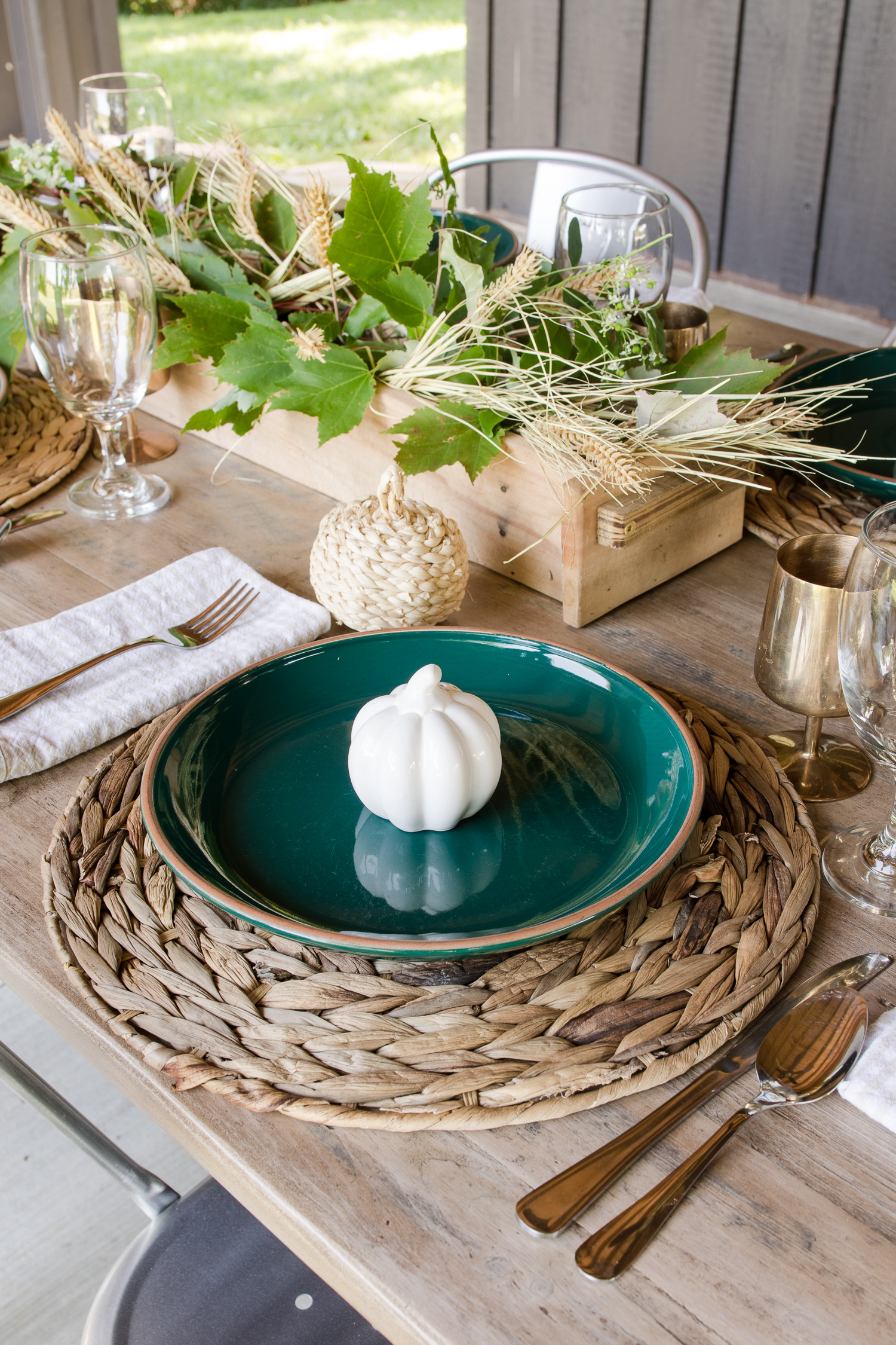 fall tablescape on the outdoor back patio with green plates, wooden table, silver metal chairs, pumpkins and brass goblets