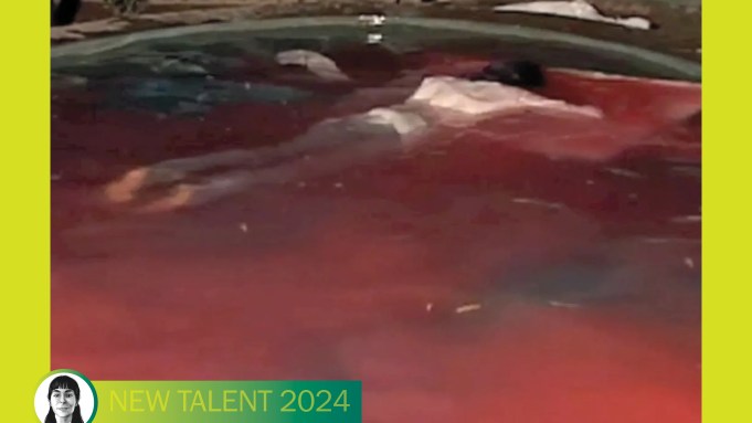 A black haired olive skinned body floats in a pool of water painted red.