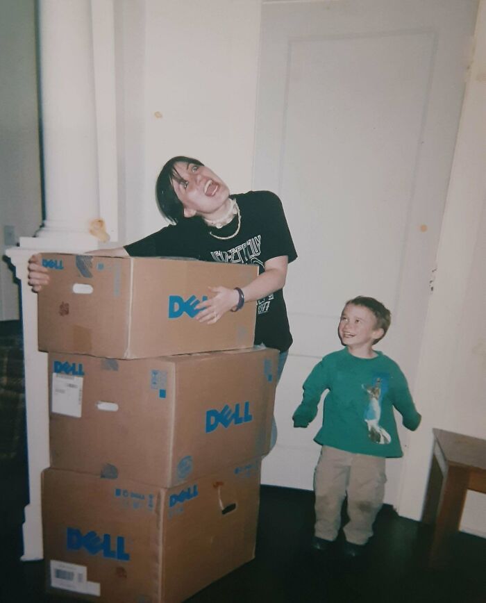 Teen laughing while stacking Dell boxes, with a smiling child nearby, depicting an awkward childhood moment.