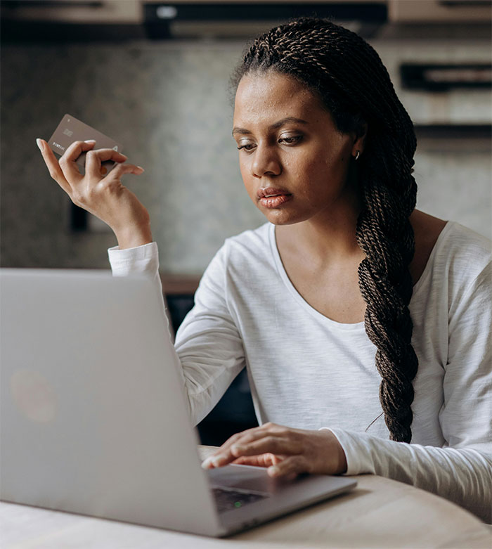 Woman persistently tracking delayed order on laptop, holding a credit card.