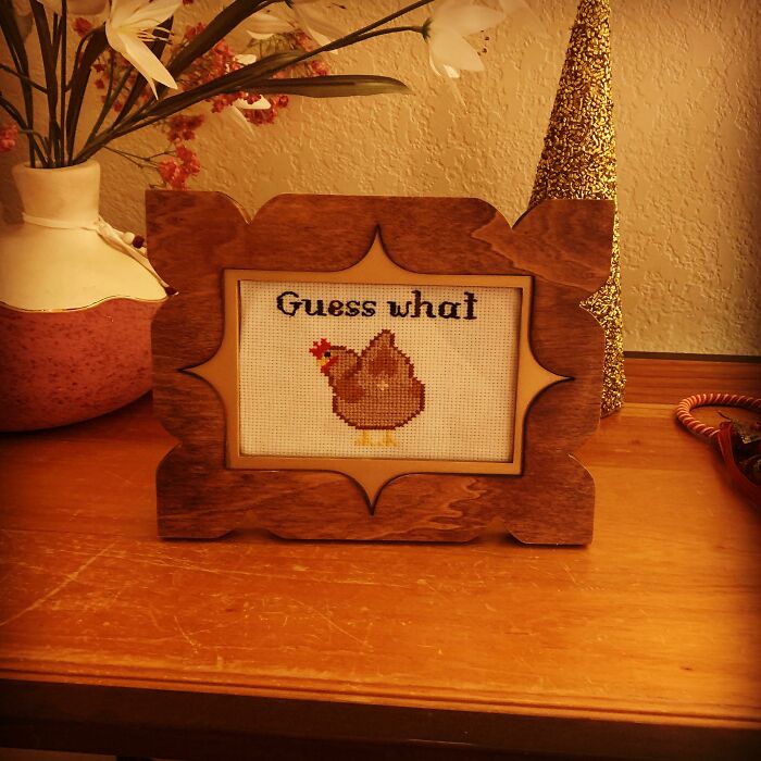 Cross-stitched chicken with "Guess what" in a wooden frame, perfect for hilarious trolling Christmas gifts.