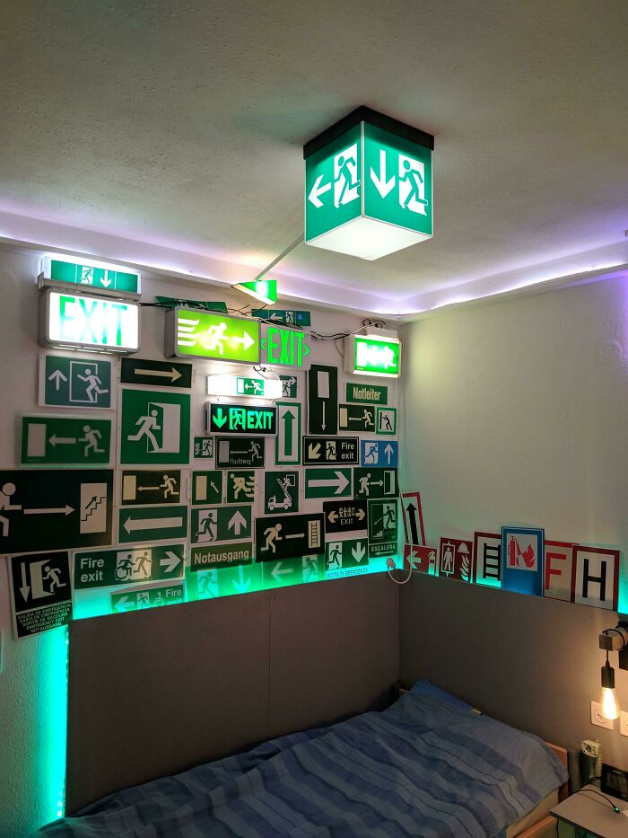 Room decorated with unique collection of various green exit signs above bed.