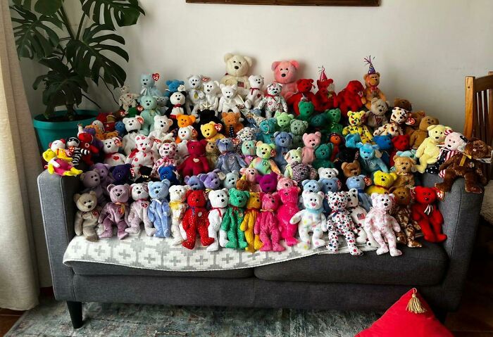 Unique collections of colorful teddy bears displayed on a grey couch in a cozy room.