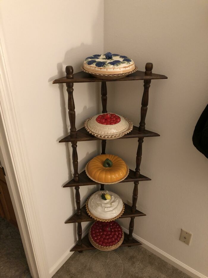 Unique collections of ceramic pies displayed on a wooden corner shelf.