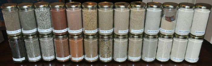 Jars of unique sand collections from various locations displayed on a table.