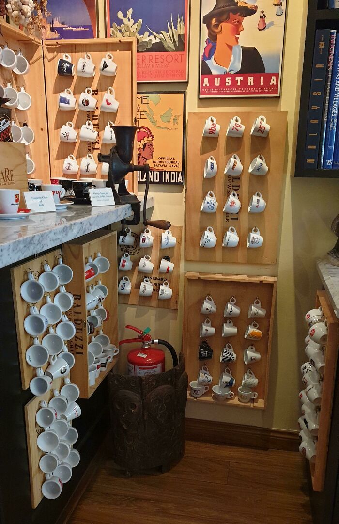 Unique collections of espresso cups displayed on wooden racks with vintage travel posters in the background.