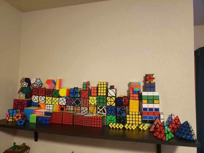 A shelf displays a collection of various colorful and uniquely shaped Rubik's Cubes.