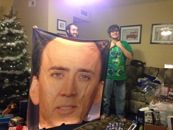 Two people laughing while holding a blanket with a large face as a hilarious trolling Christmas gift.