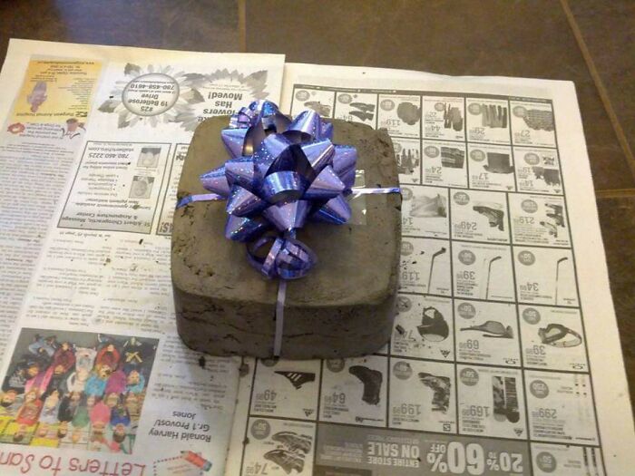 Concrete block wrapped with a purple bow, representing a humorous trolling Christmas gift set on newspaper.