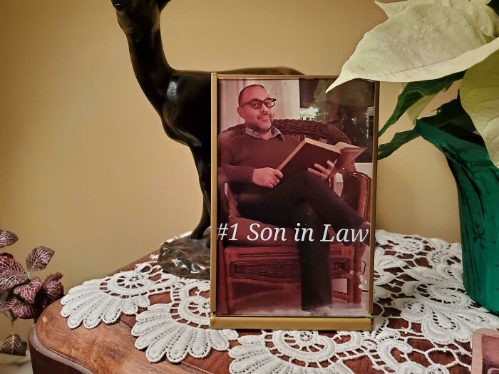 Man holding a book in a "#1 Son in Law" photo, a humorous trolling Christmas gift displayed on a decorative table.