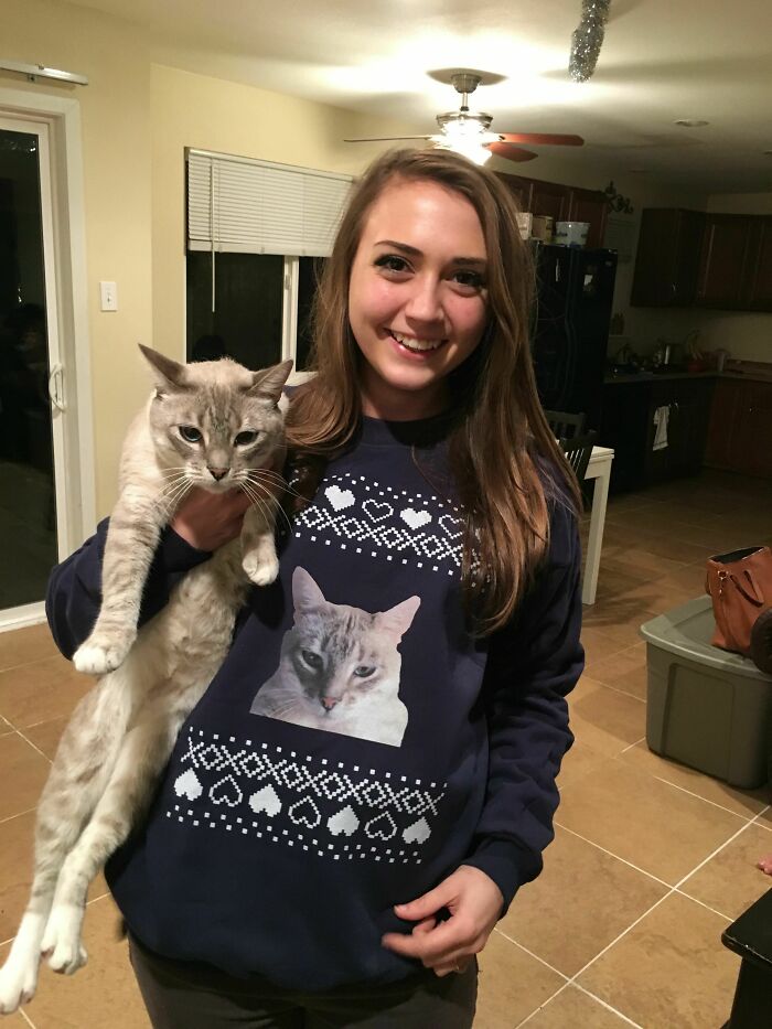 Woman holding cat, wearing sweater with funny cat picture. Perfect example of trolling Christmas gifts.